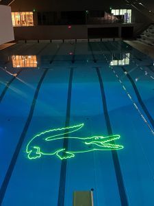 Photo of a swimming pool with a logo in the shape of a crocodile (Lacoste) projected at the bottom of the water