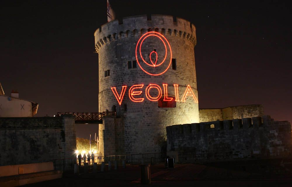 Photo of a tower at night with the Veolia logo projected on it in red