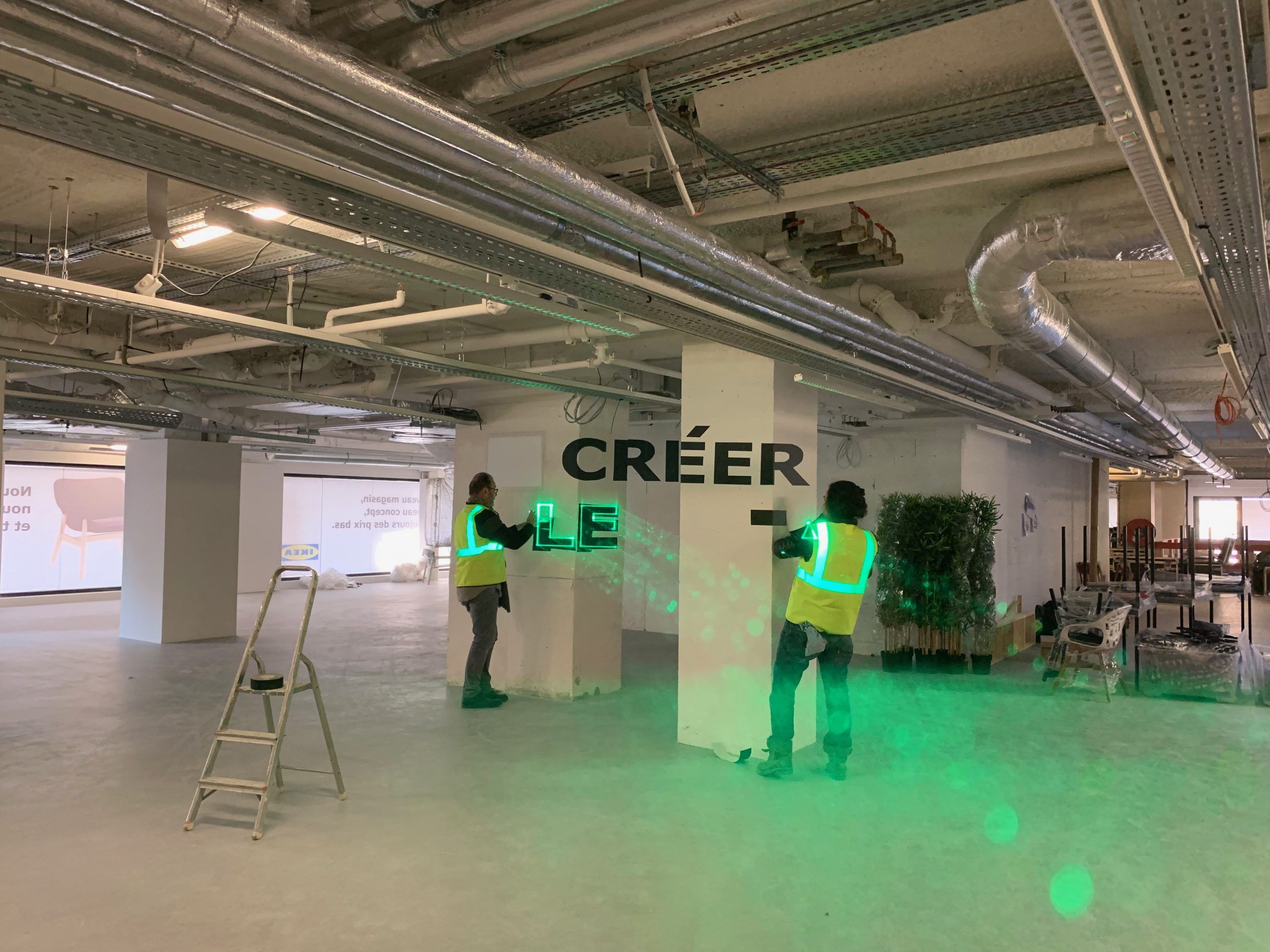 Photo of an underground car park with two people painting letters on the walls following the design projected by lasers