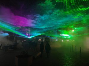 Photo of a city center with blue, green and pink colored smoke projecting into the sky