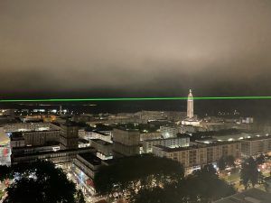 Photo of a green laser beam projected into the sky of a city