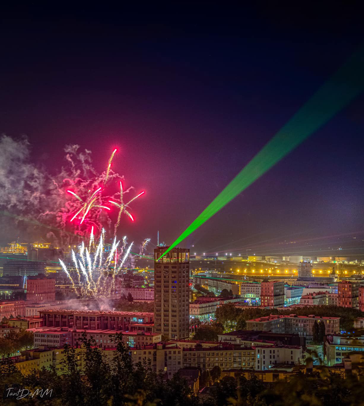 Photo of a tower with green laser beam coming from the tower and fireworks