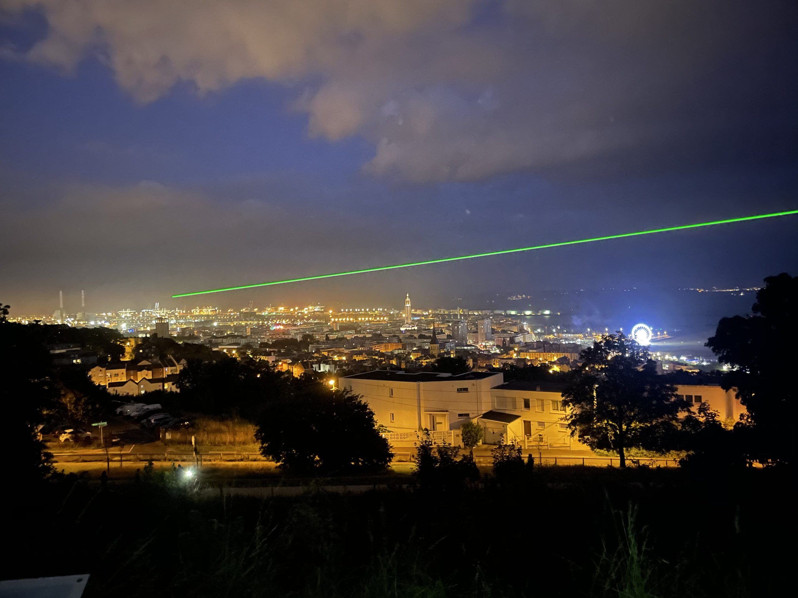 Photo of a green laser beam projected into the sky of a city