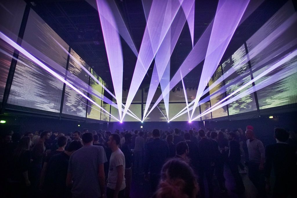 Photo of a concert with purple laser beams crossing the room