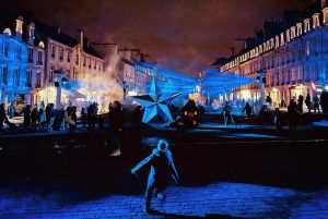 Photo of the city center of Caen with blue laser beams and a star-shaped structure in the center