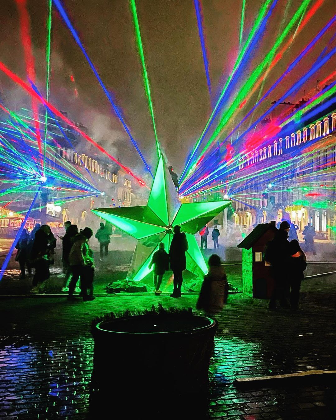 Photo of the city center of Caen with blue, green and red laser beams and a star-shaped structure in the center
