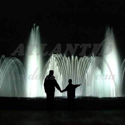 Europe Évènement - Photo d'une fontaine avec des jets d'eau blancs et les ombres d'un homme tenant la main d'un enfant devant