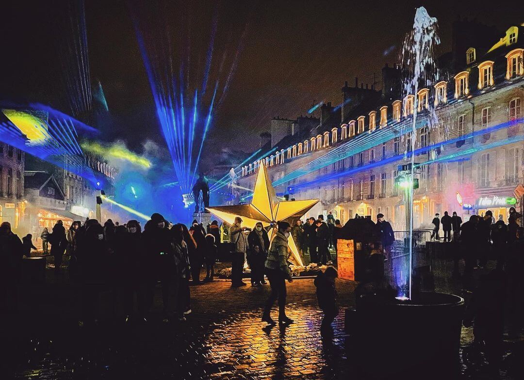 Europe Évènement - Photo du centre ville de Caen avec des faisceaux lasers bleus et une structure en forme d'étoile au centre jaune