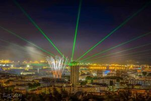 Europe Évènement - Photo of a city tower with projection of green laser beams from the tower and fireworks in Le Havre