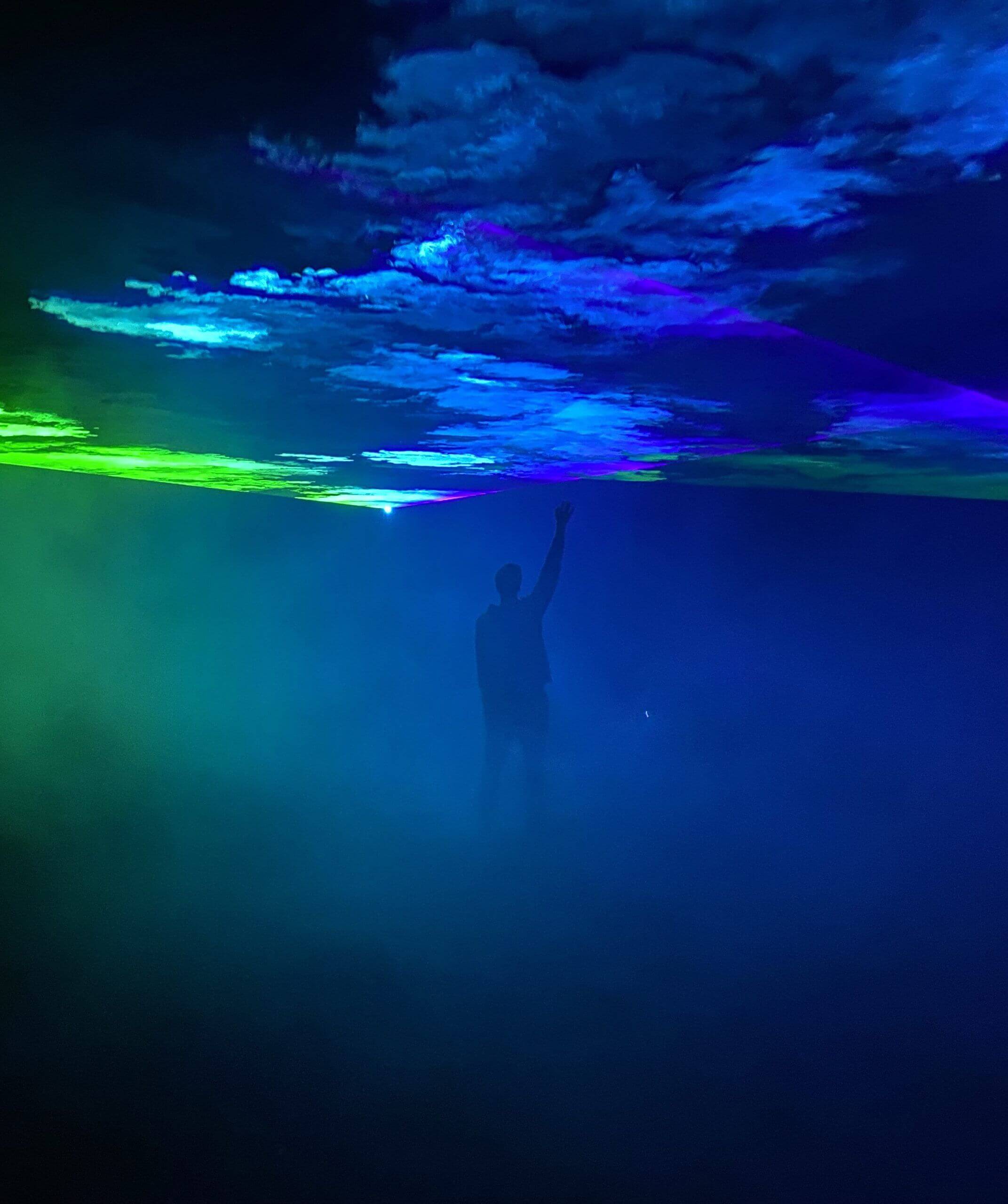 Europe Évènement - Photo d'un homme levant la main pour toucher la projection de fumée bleu et verte lors d'un spectacle laser
