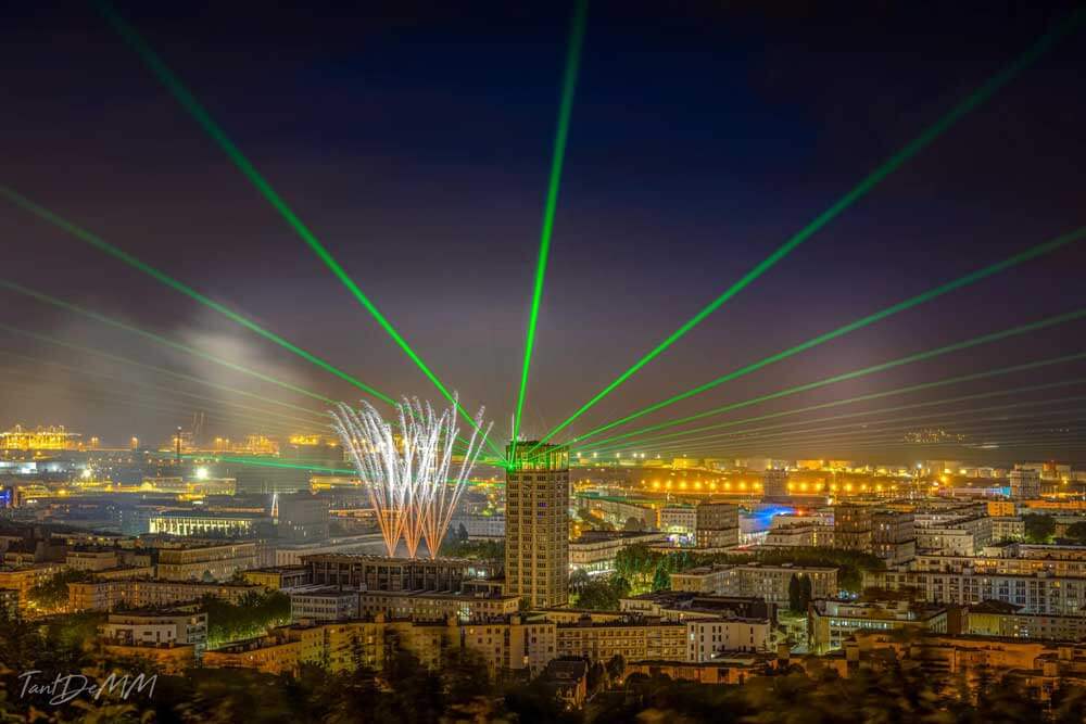Europe Évènement - Photo d'une tour dans une ville avec des feux d'artifices et des faisceaux lasers verts de projeter au Havre